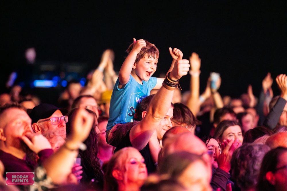 Children enjoying live music at a Moray Events concert, with an enthusiastic crowd, colourful lighting, and a lively atmosphere at the outdoor event.